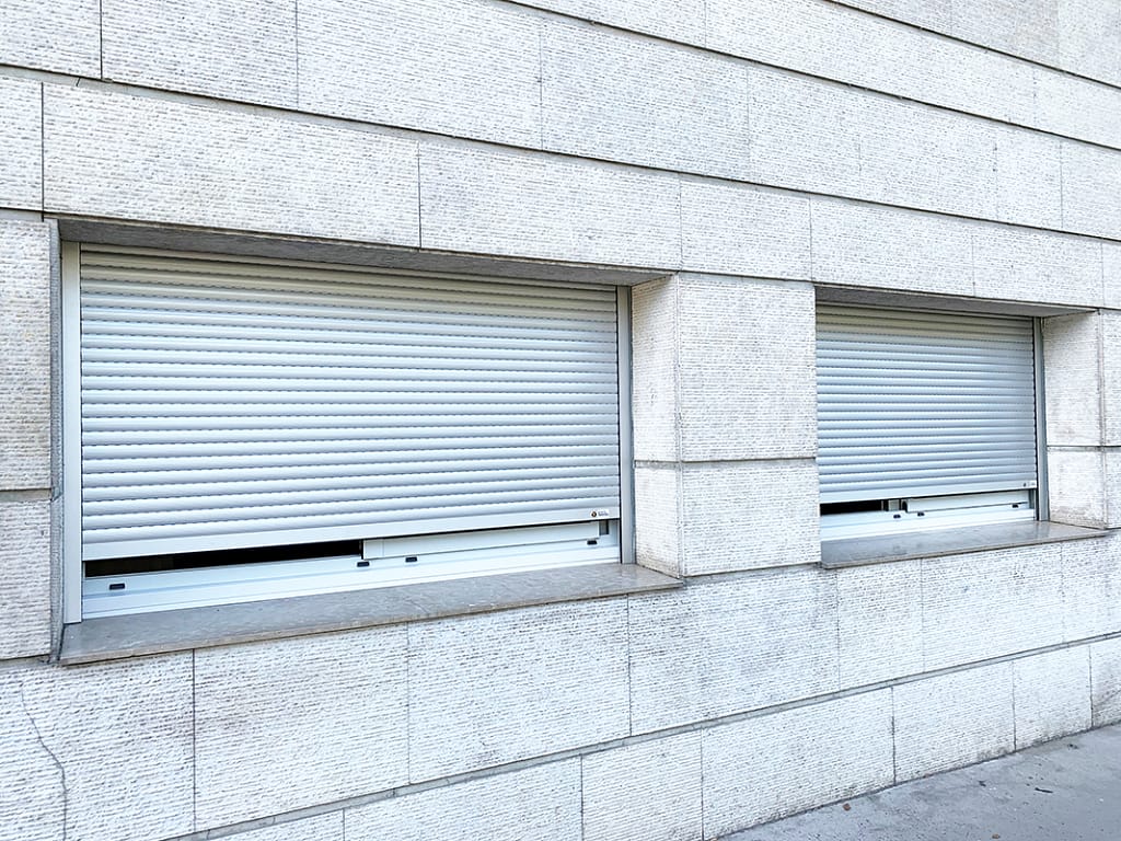 Fenêtre isolée avec un volet roulant baissé tradilux en alu blanc de la marque Flip, sur une façade en pierre blanche