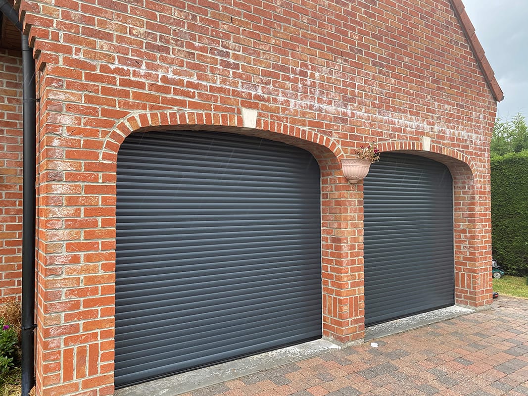 Double porte de garage enroulable Dooralux noir sur un mur en brique rouge