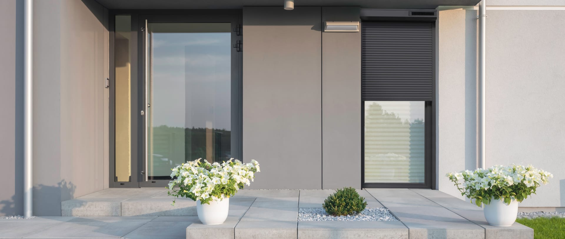 Vue depuis la terrasse d'une maison moderne grise avec des volets roulants noirs et deux pots de fleurs blanc
