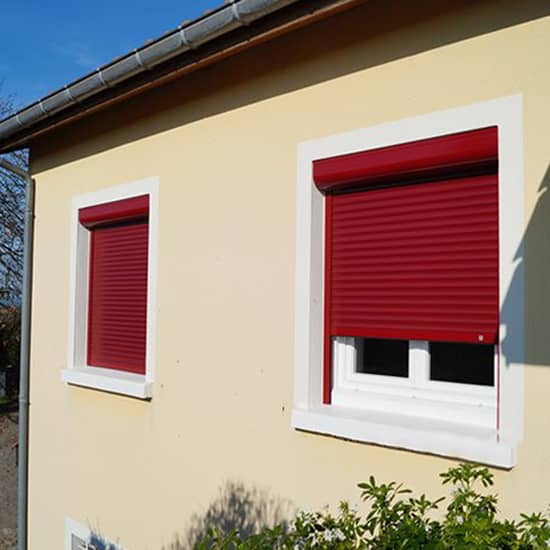 Façade d'une maison beige avec des fenêtres aux volets roulants rouge astrolux renolux de la marque Flip
