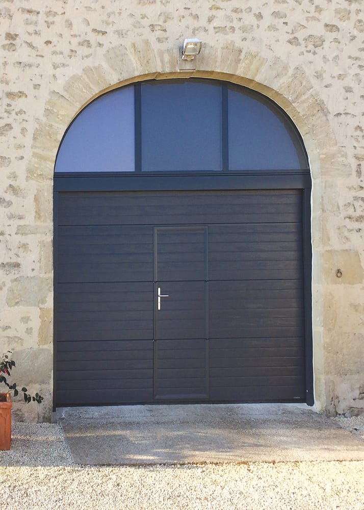 Porte de garage sectionnelle plafond noire isolée sur un mur en pierre avec un portillon