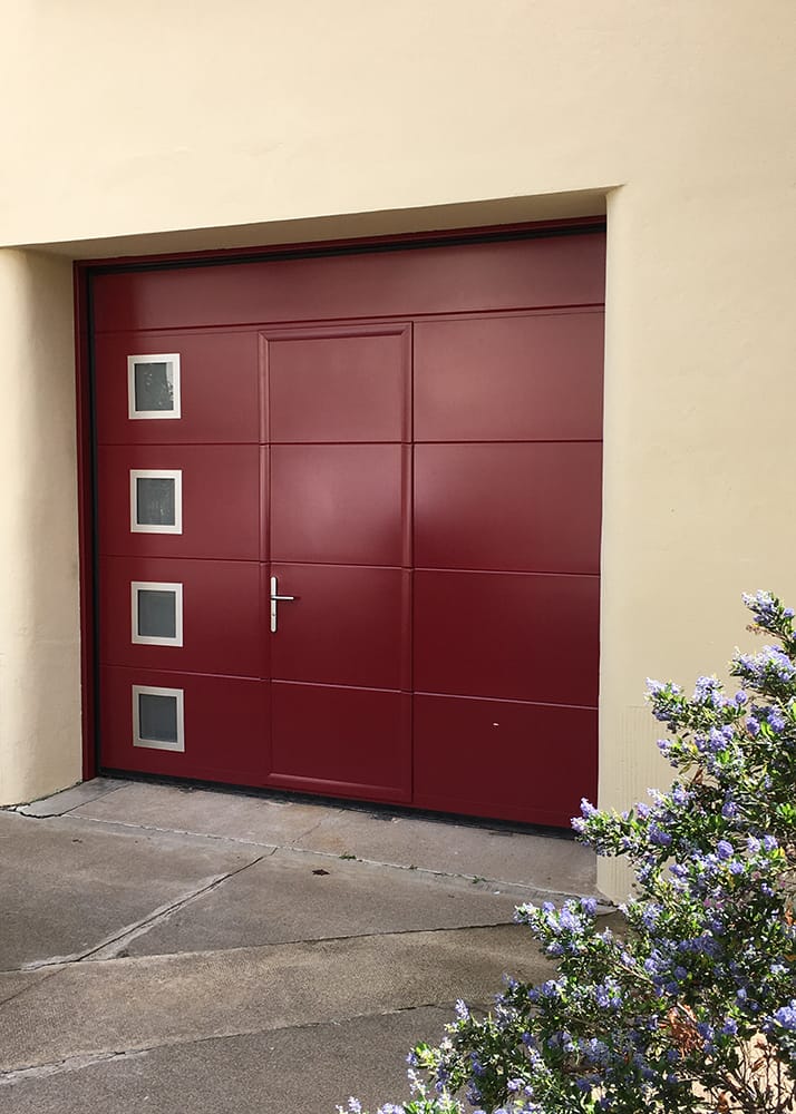 Porte de garage sectionnelle plafond rouge avec portillon et des hublots