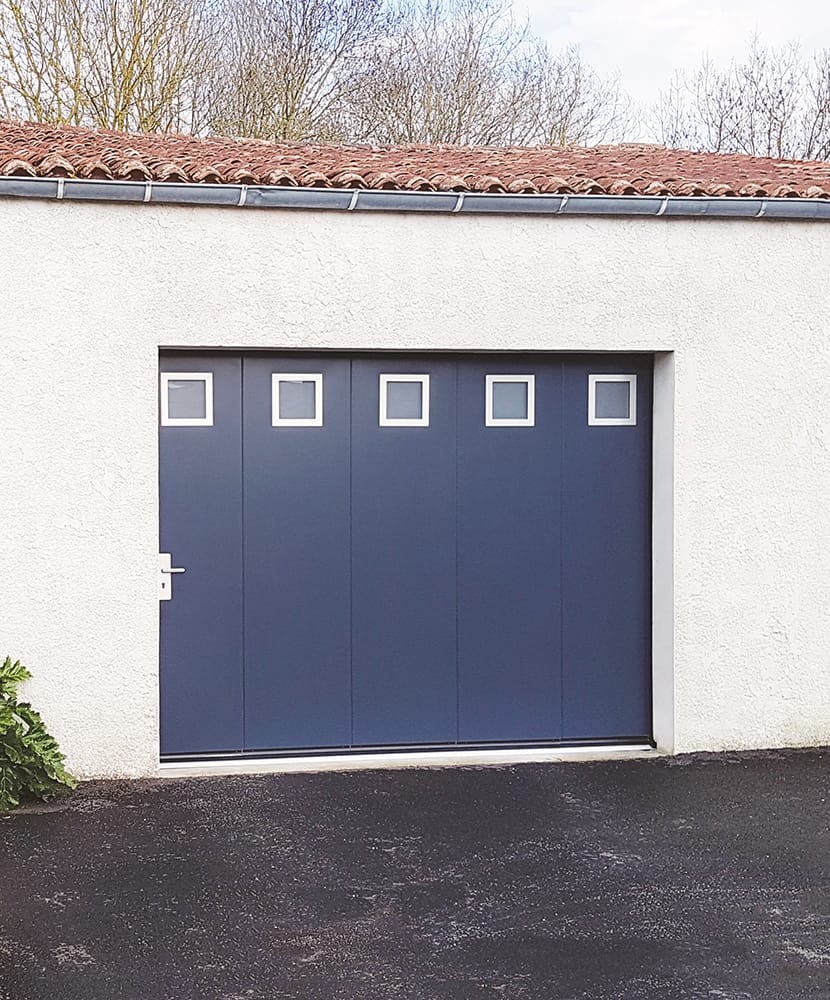 Porte de garage sectionnelle latérale bleue avec portillon et hublot carrés, maison mur crépis blanc
