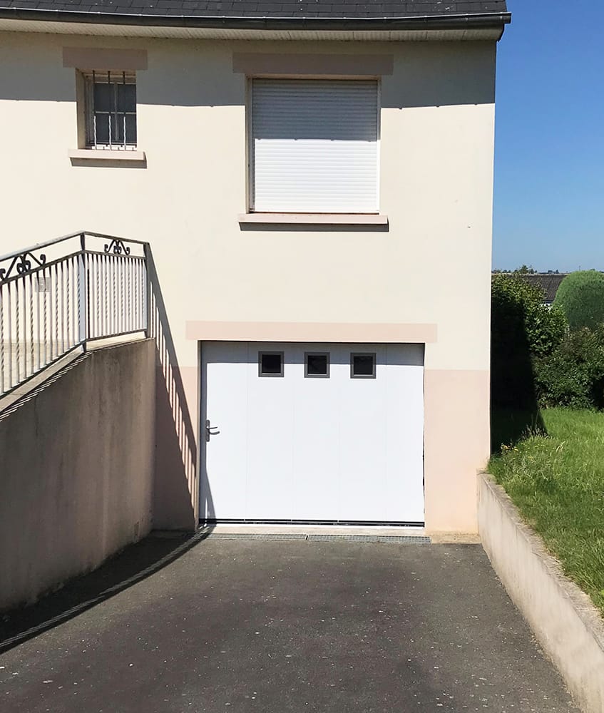 Porte de garage sectionnelle latérale blanche avec des hublots sur une maison beige