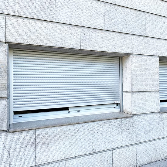 Fenêtre isolée avec un volet roulant baissé tradilux en alu blanc de la marque Flip, sur une façade en pierre blanche